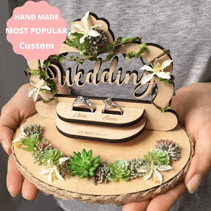 a person holding a piece of wood that says wedding on it with succulents and greenery