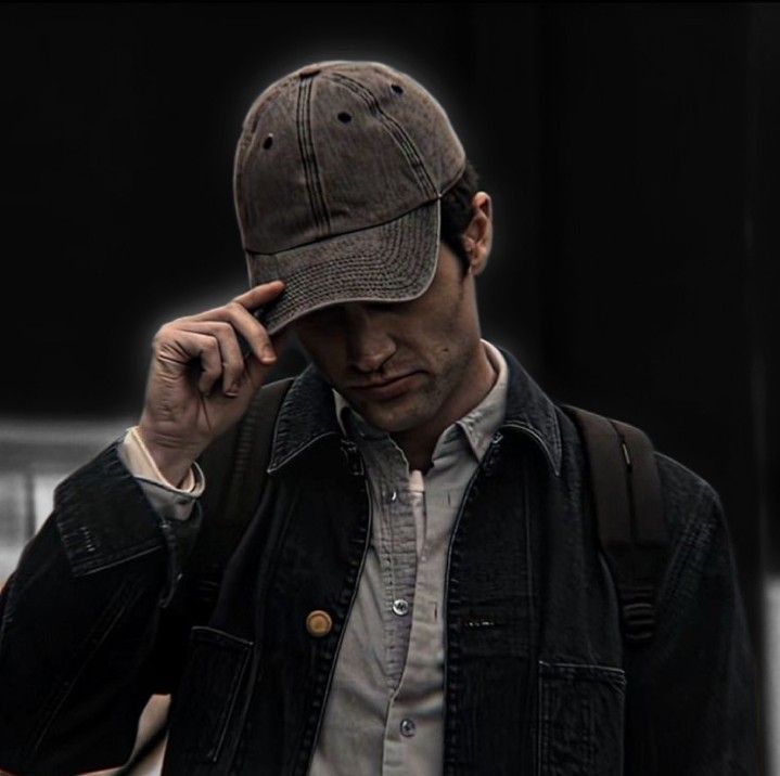 a man wearing a hat while holding his hand to his ear and talking on the phone