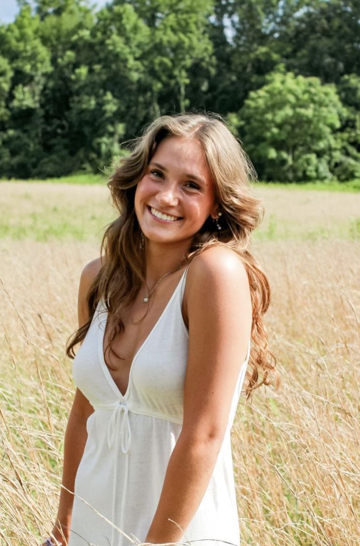 a woman in a white dress is standing in tall grass and smiling at the camera