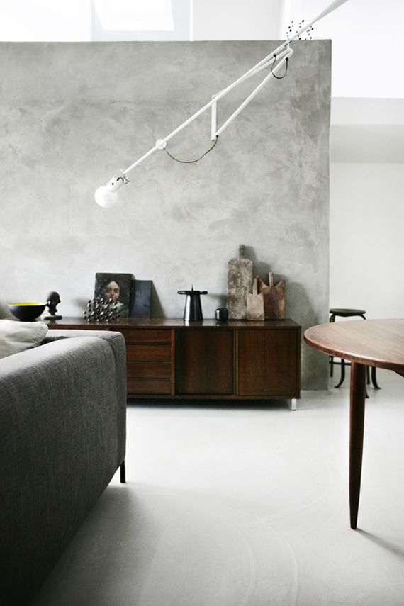 a living room filled with furniture and a lamp on top of a wooden table in front of a gray wall