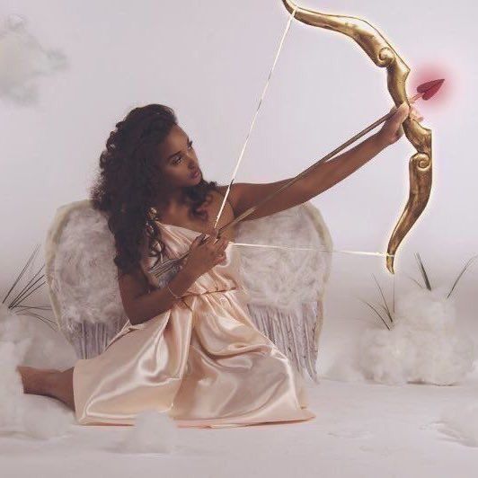 a woman in a pink dress is holding a bow and arrow while sitting on a white chair