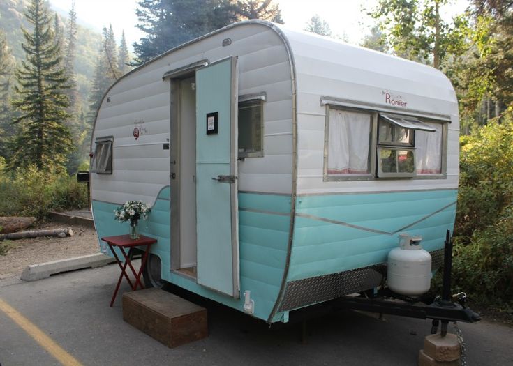 an old camper trailer is parked on the side of the road in front of some trees