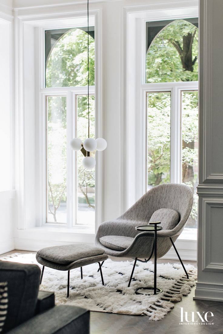 a chair and ottoman are in front of two large windows, one is gray the other is white