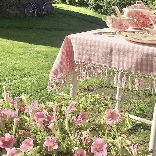 a table with pink flowers and plates on it in the grass next to a potted plant