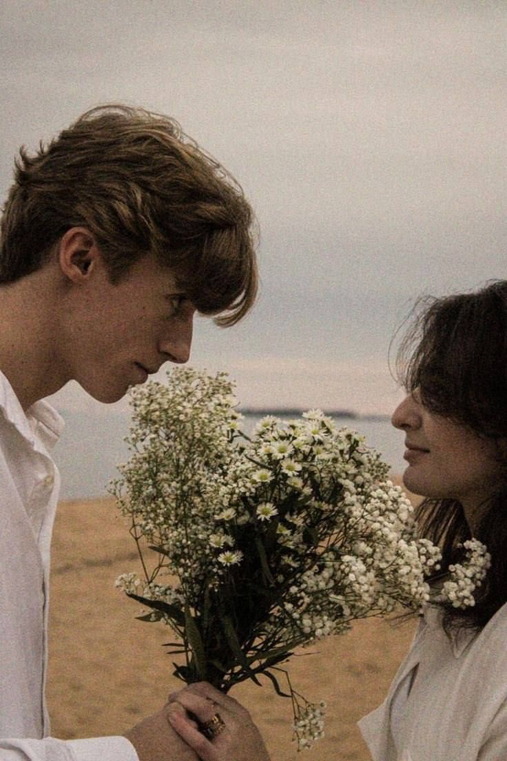 a man and woman standing next to each other on a beach with flowers in their hands