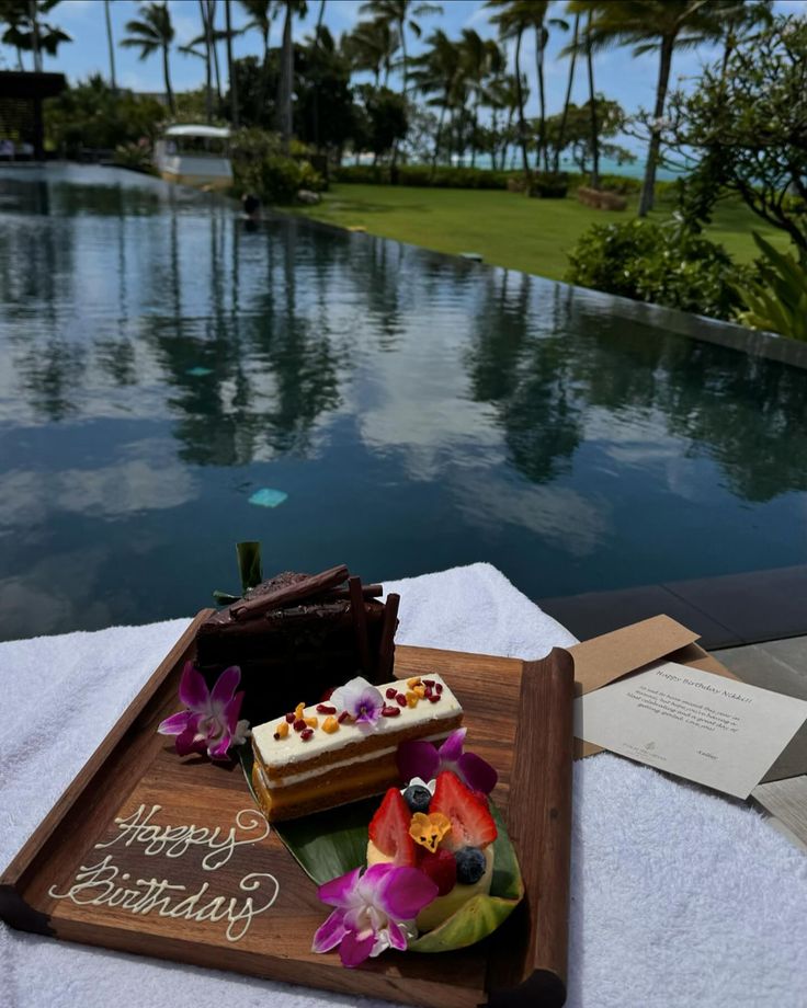 there is a piece of cake on the table next to the pool and some flowers