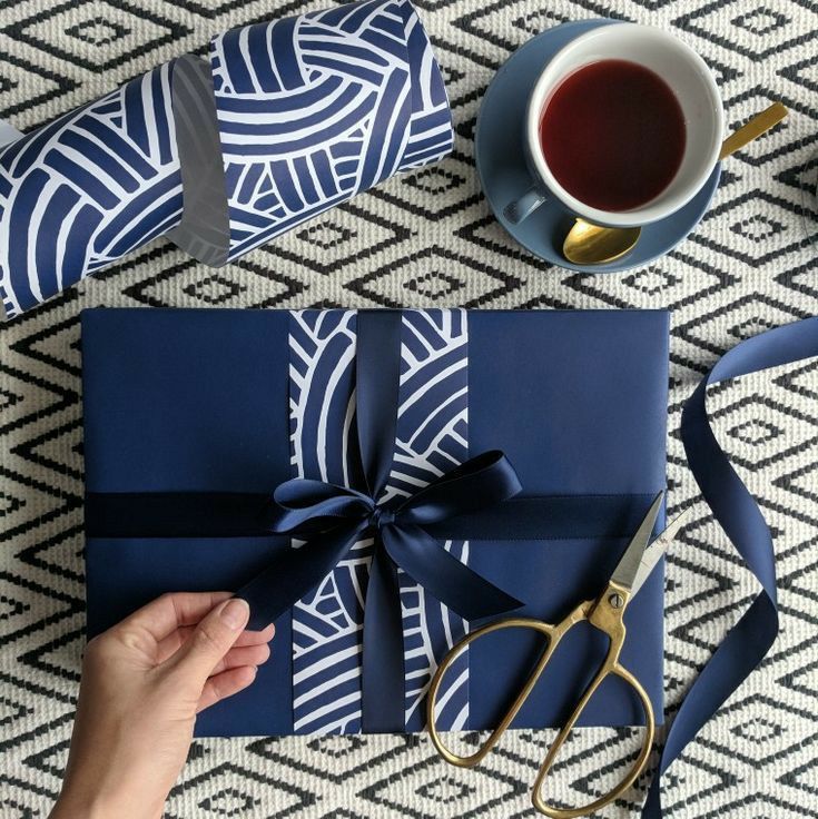 a person opening a blue gift box on top of a table next to a cup of coffee