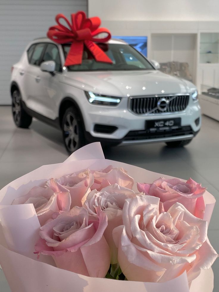 a bouquet of pink roses sitting in front of a white car with a red bow on it