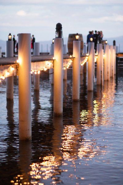 people are standing on poles in the water with lights strung from them and floating around