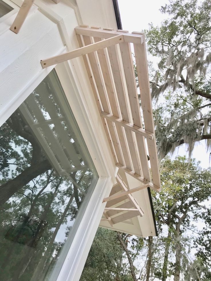 a wooden ladder hanging from the side of a house next to a window with trees in the background