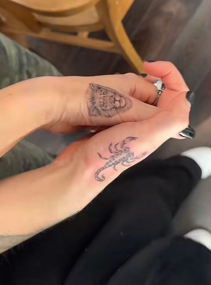 two people with tattoos on their fingers and one holding the other's hand while sitting down