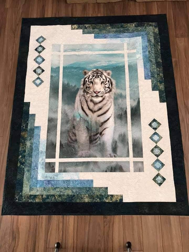 a white tiger sitting on top of a wooden floor next to a wall mounted quilt