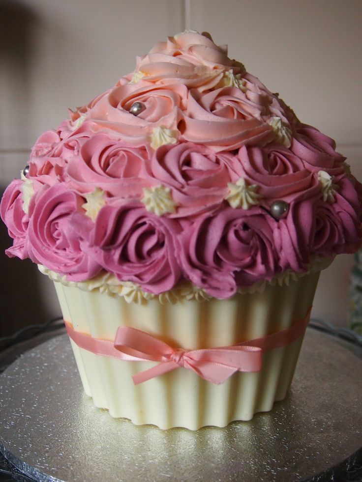 a large cupcake with pink frosting and flowers on it's top sitting on a table