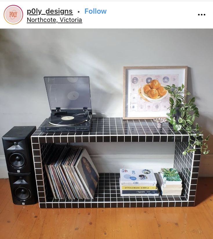 a record player sitting on top of a black shelf next to a plant and records