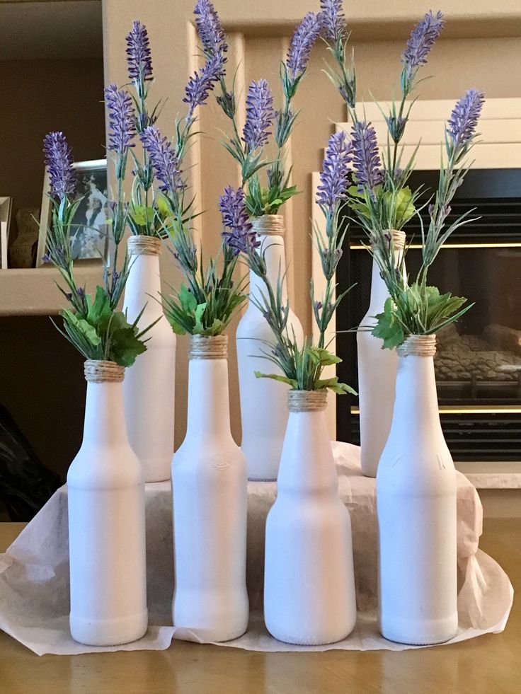 six white bottles with lavender flowers in them on a table next to a fire place