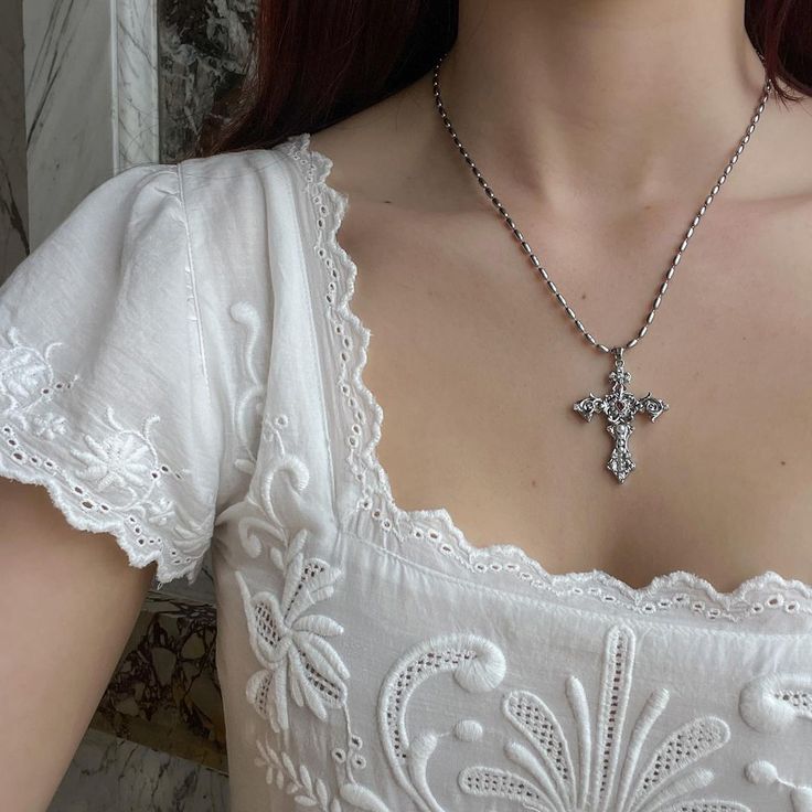 a woman with red hair wearing a white dress and a cross necklace on her neck