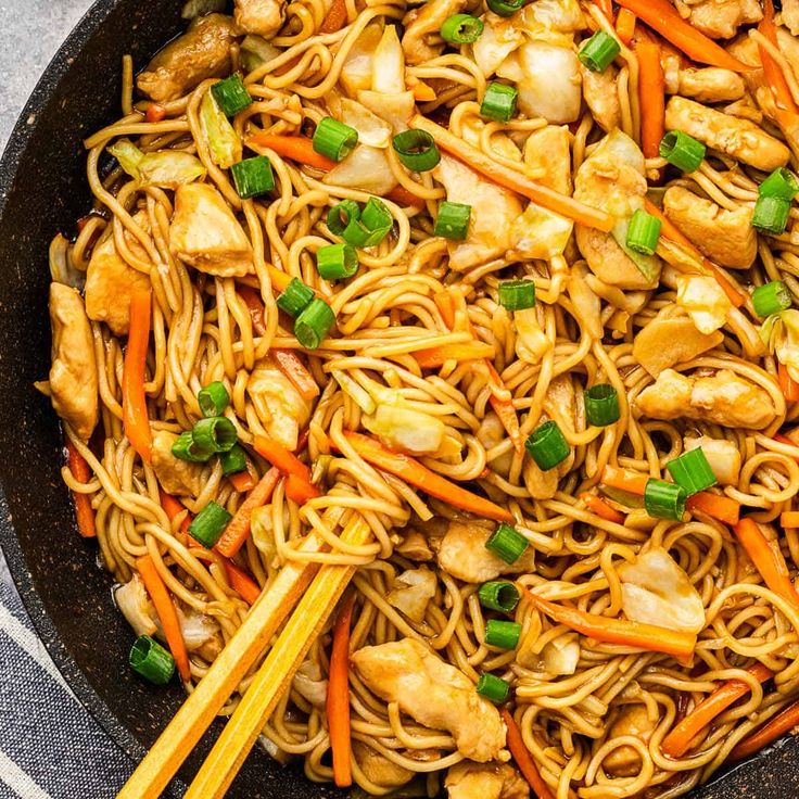 chicken lo mein with carrots and green onions in a wok on the table