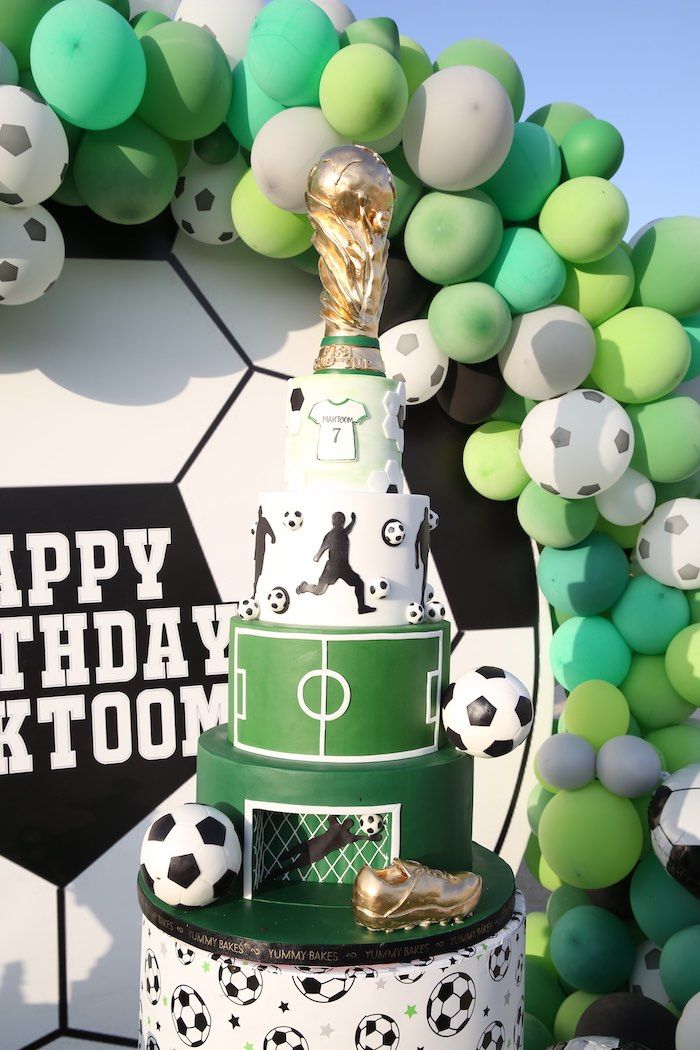 a soccer themed birthday cake is displayed in front of a backdrop with green and white balloons