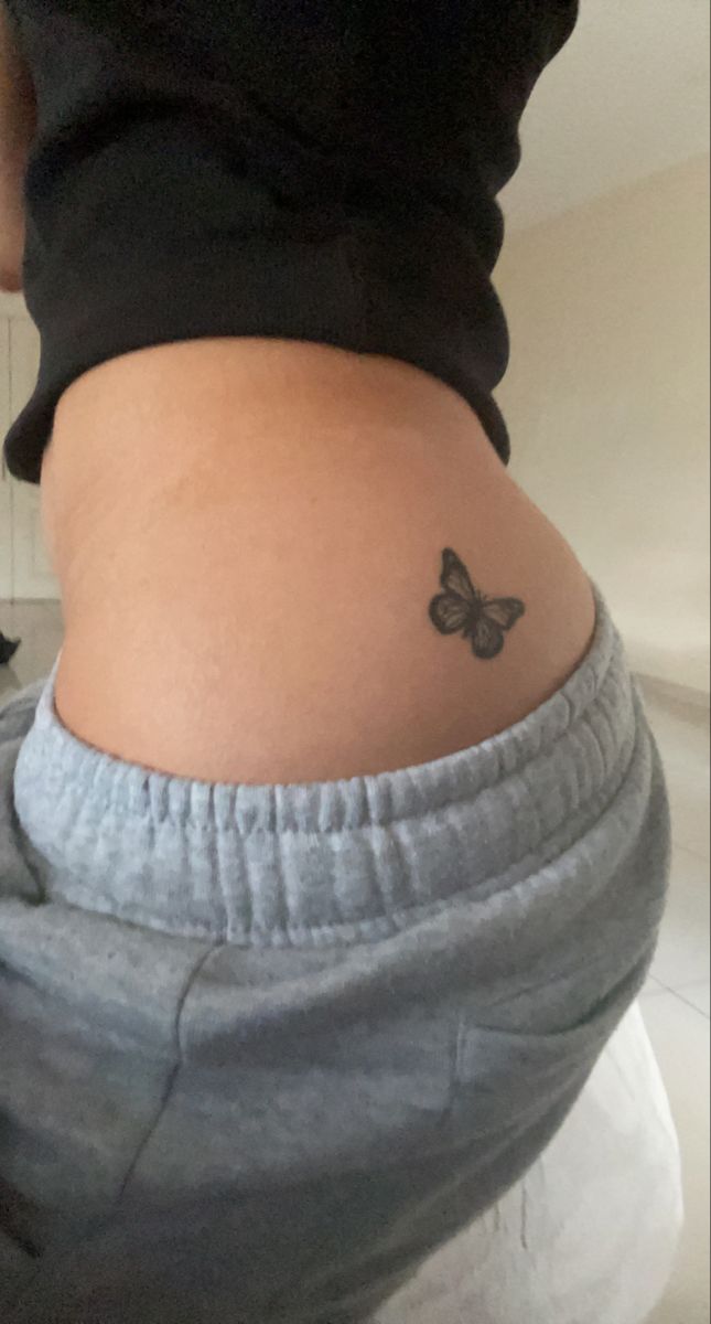 a woman with a small butterfly tattoo on her lower back side ribcacture