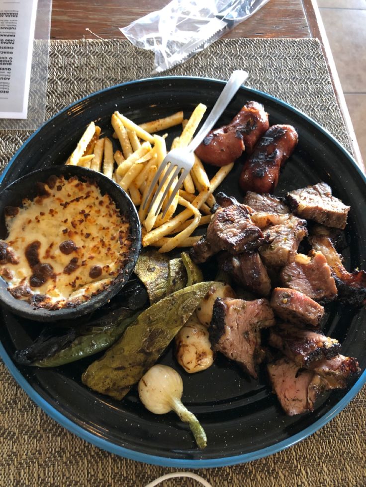 a black plate topped with meat and fries next to a bowl of sauce on top of a table