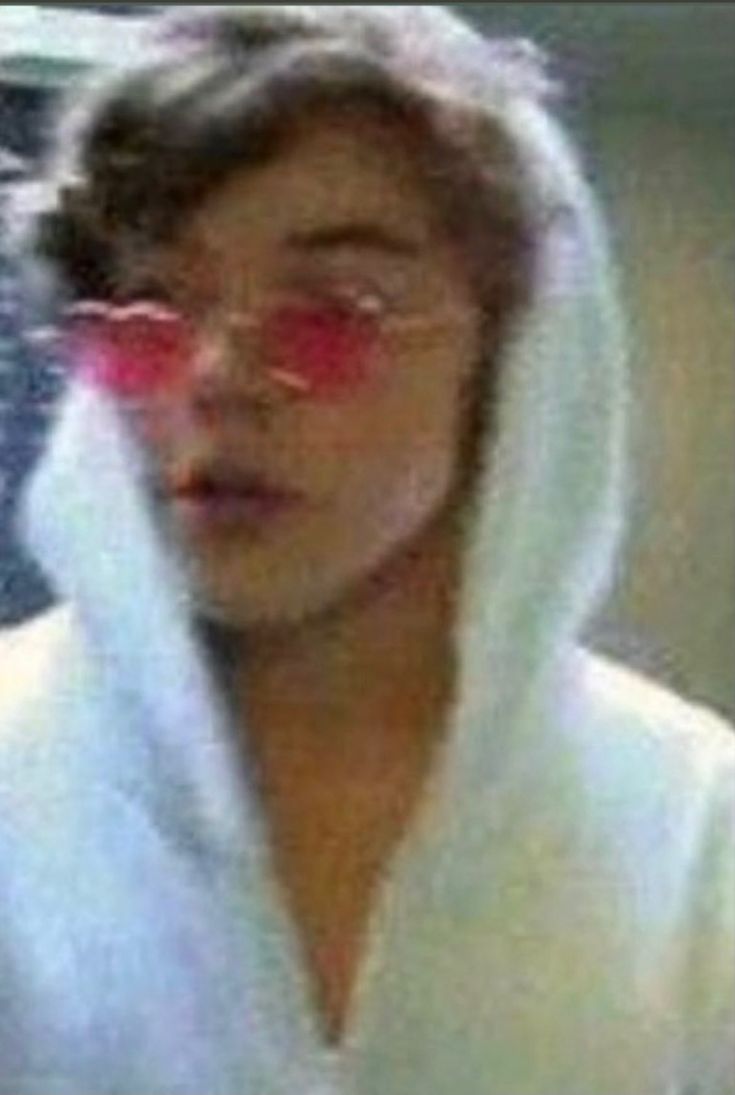 a blurry image of a woman wearing sunglasses and a white hoodie with red tinted glasses