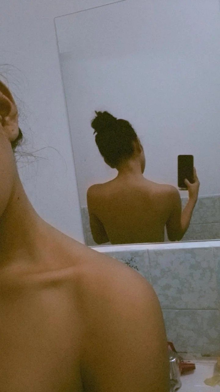 a woman taking a selfie in front of a bathroom mirror with her back turned to the camera