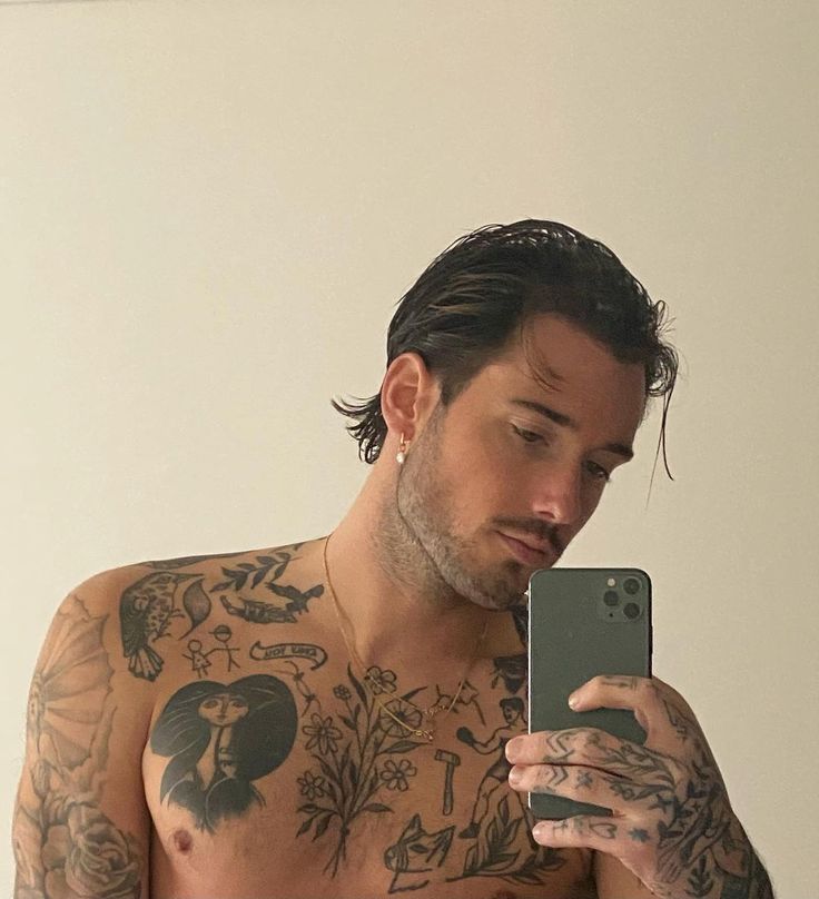 a man with tattoos is looking at his cell phone and holding it up to the camera