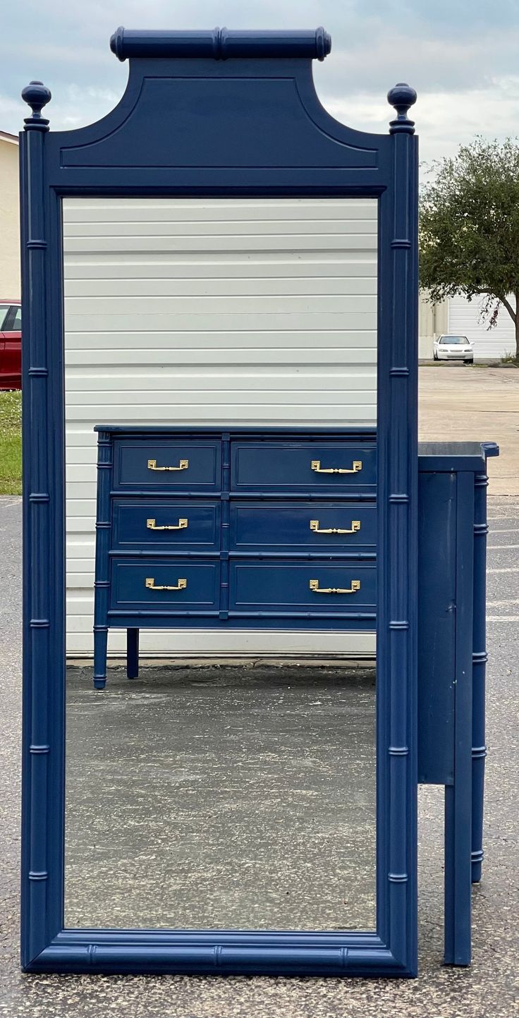 a blue dresser sitting in front of a mirror on top of a parking lot next to a building