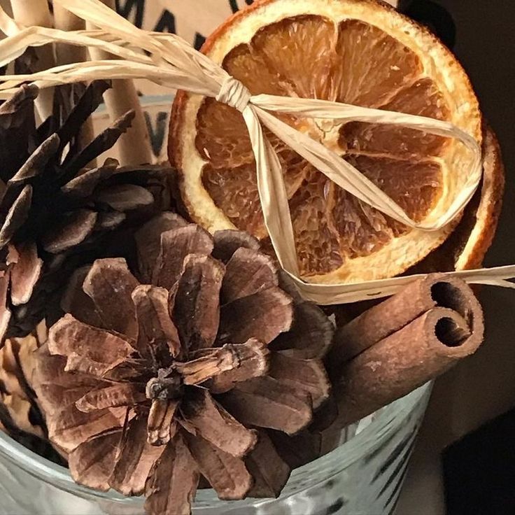 pine cones, oranges and cinnamon sticks are arranged in a bucket