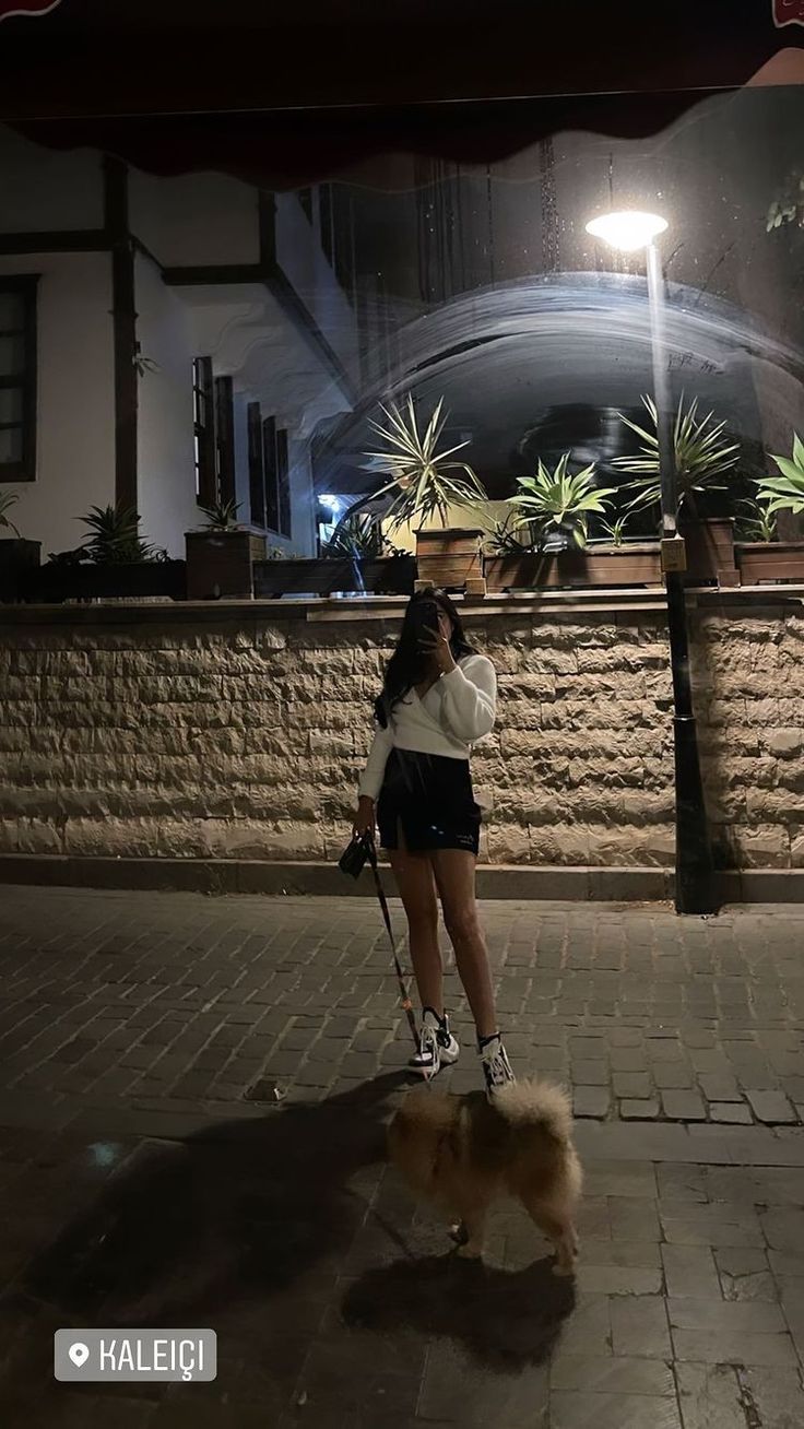 a woman is standing on the sidewalk at night with her cell phone up to her ear