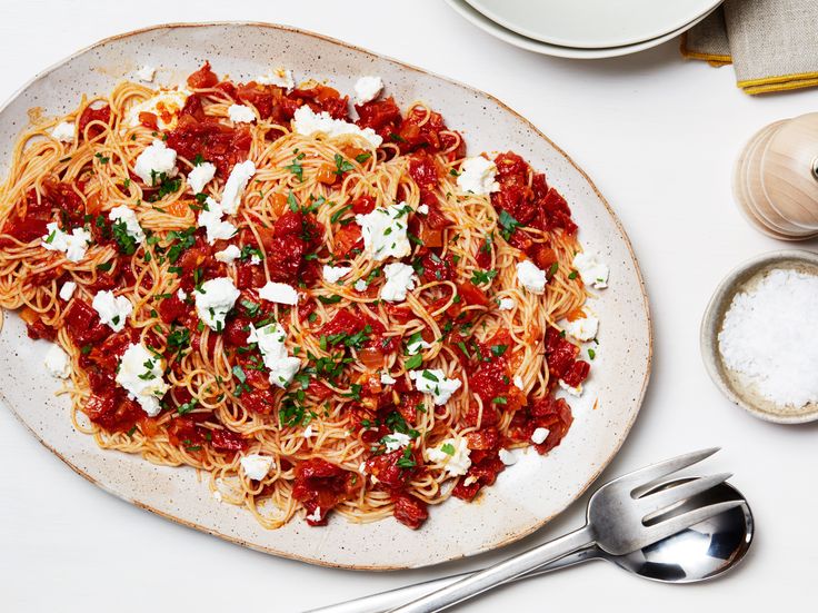 a plate of spaghetti with tomato sauce and fettuccine on it next to two silver spoons