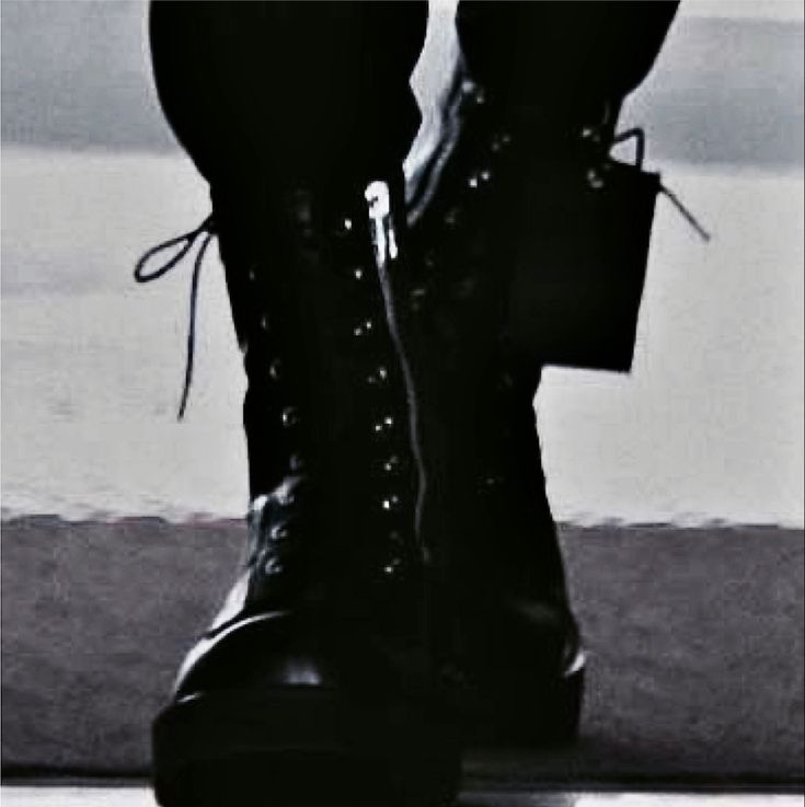 black and white photograph of someone's legs wearing boots with laces on them