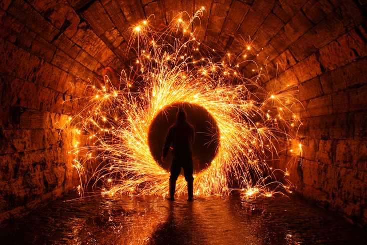 a person standing in front of a tunnel filled with fire and sparkles at night