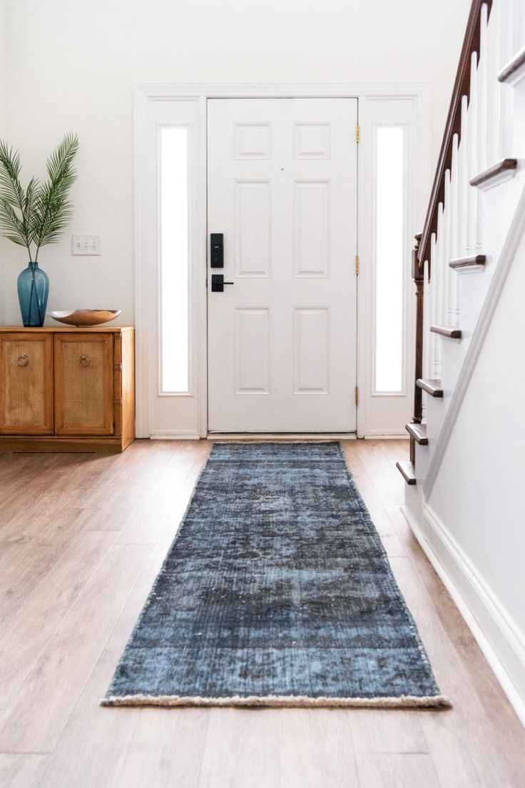 a blue rug on the floor in front of a white door and wooden stairs with potted plant