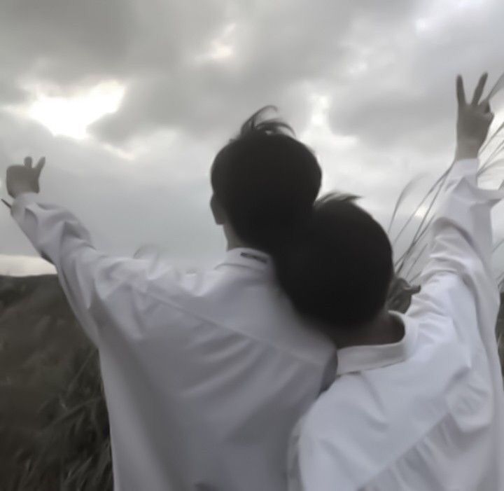 a woman with her arms outstretched in front of the sky and grass, while another person holds their hands up