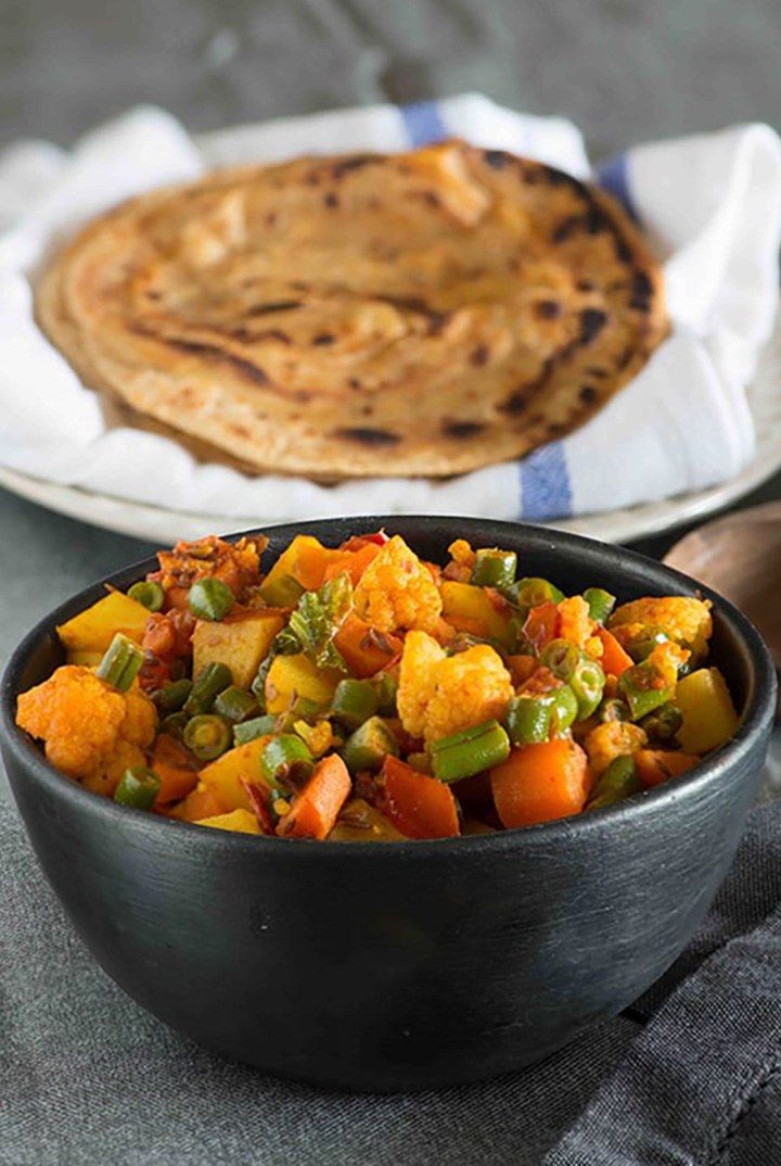 two bowls filled with food sitting on top of a table next to a flatbread