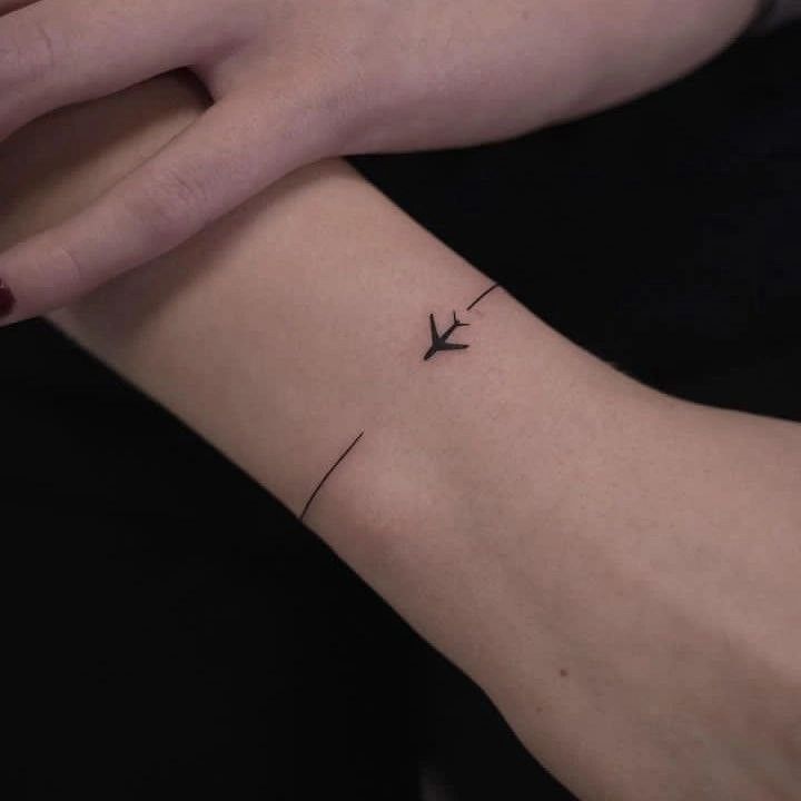 a woman's arm with a small airplane tattoo on the left side of her wrist