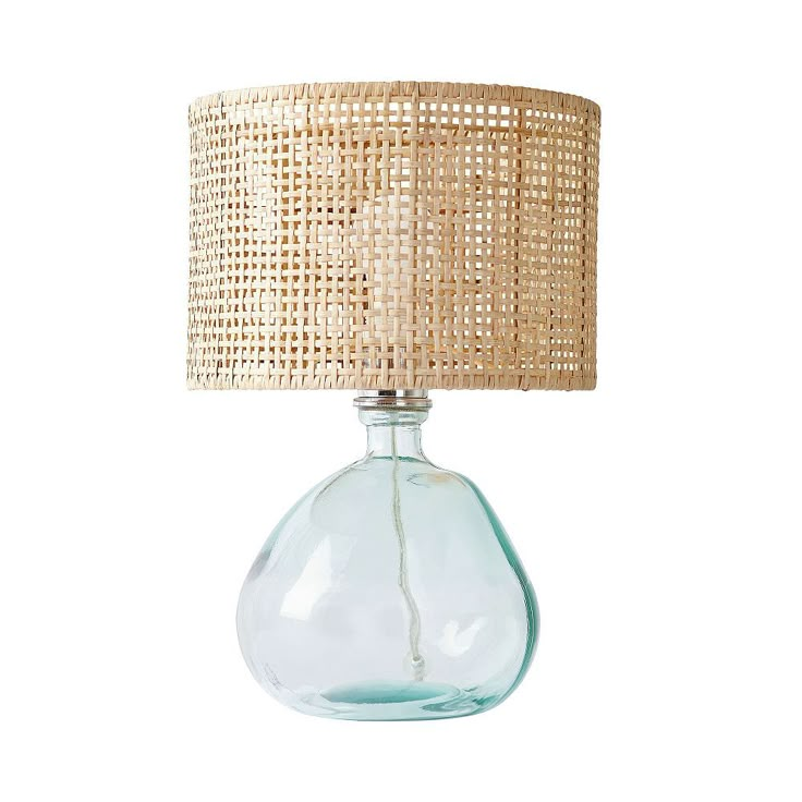 a glass table lamp with a woven shade on the base and a light bulb attached to it