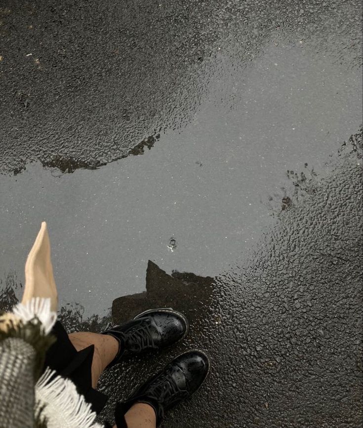 a person's feet in black shoes standing on wet pavement