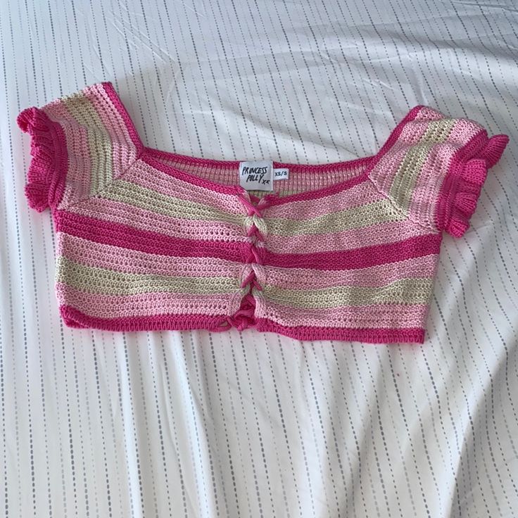 a pink and white striped sweater laying on top of a bed next to a pillow