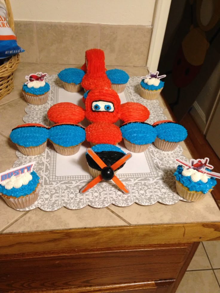 an airplane cupcake with blue frosting and red icing on it, surrounded by other cupcakes