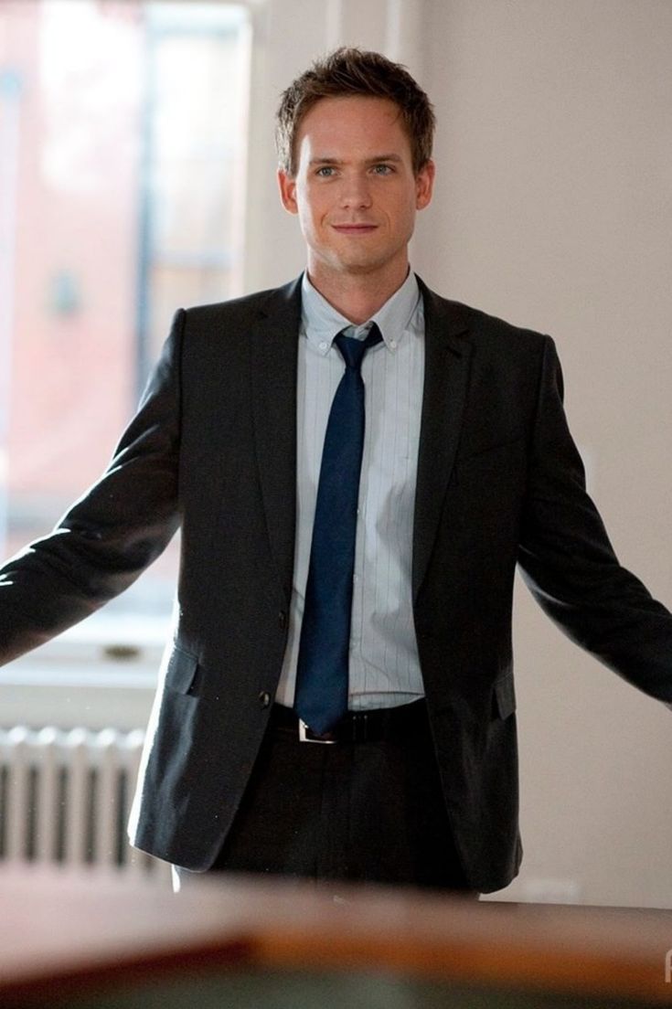 a man wearing a suit and tie standing in front of a window with his hands out