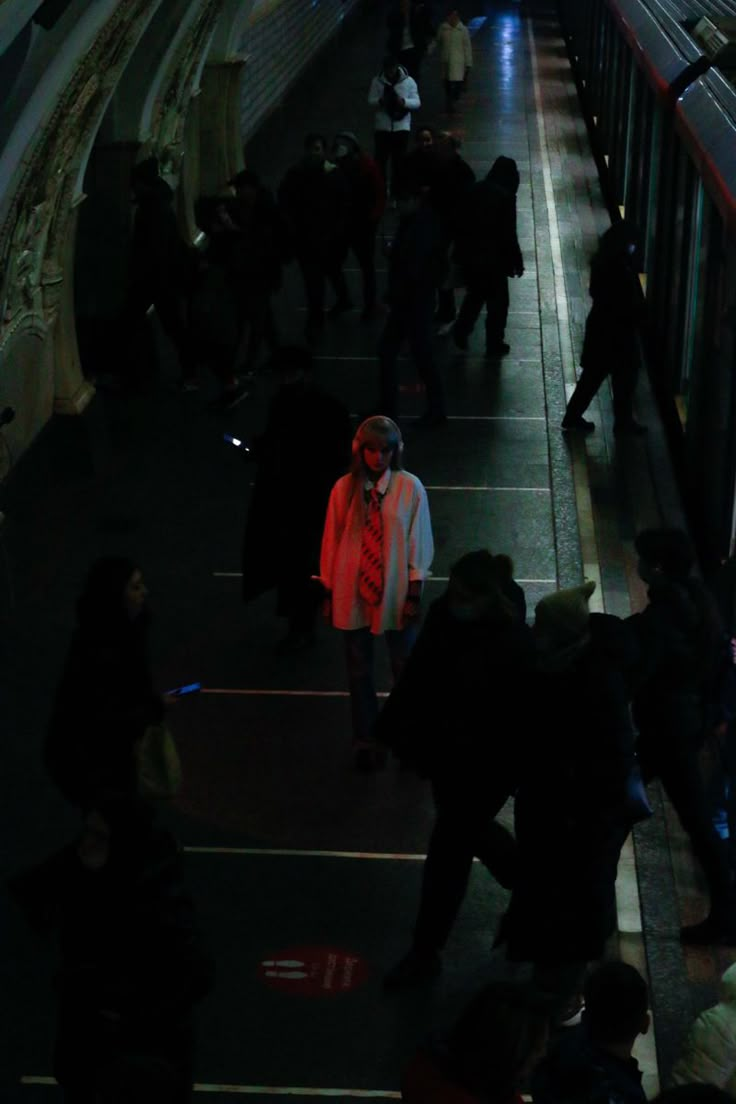 many people are walking on the subway platform at night, with one person wearing an orange jacket