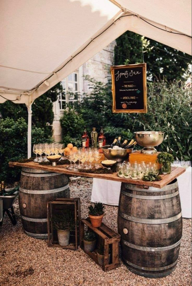 an outdoor bar with wine glasses and bottles on it, surrounded by potted plants