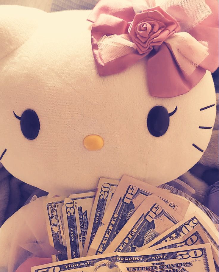 a hello kitty stuffed animal with money in its lap and pink bow on it's head