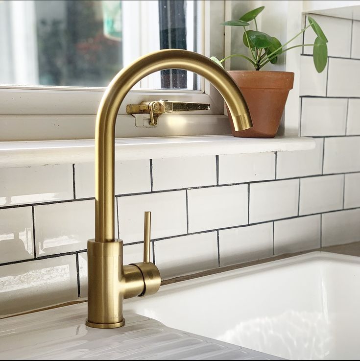 a gold faucet on a white kitchen counter next to a potted plant