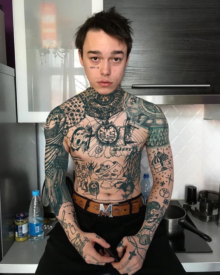 a tattooed man sitting on top of a kitchen counter