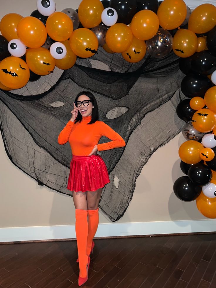 a woman in an orange shirt and red skirt standing next to balloons with eyes on them