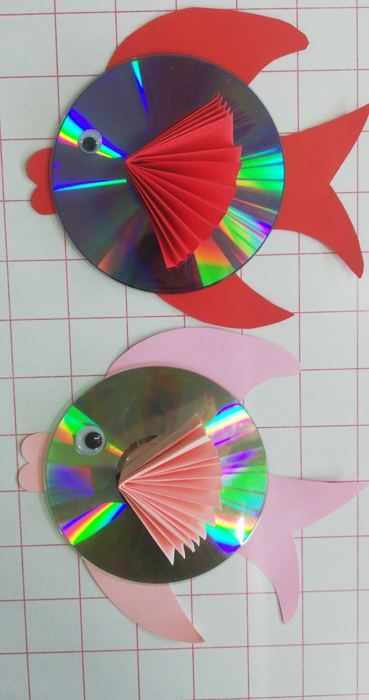 two fish made out of cd's sitting on top of a cutting mat next to each other