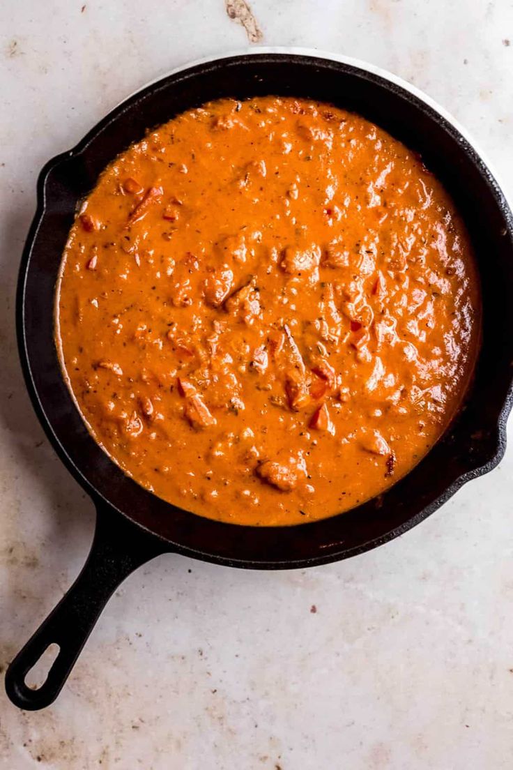 a skillet filled with red sauce on top of a white countertop next to a wooden spoon